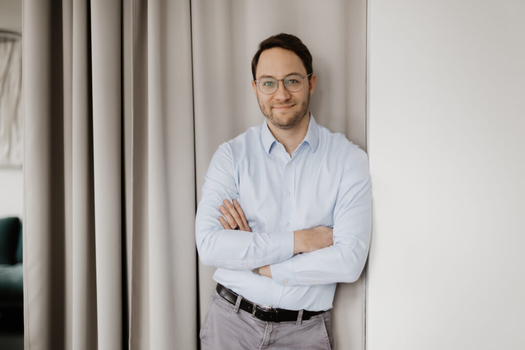 Dr. Thomas Bacharach Experte für Darmgesundheit in hellem Hemd und Jeans lächelnd locker an die Wand gelehnt