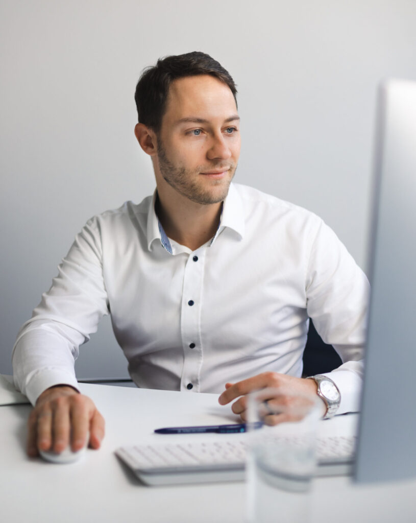 Dr. med. Thomas Bacharach, Experte für Sibo und Darmgesundheit, in heller Umgebung und weißem Hemd arbeitet an seinem Computer am Schreibtisch